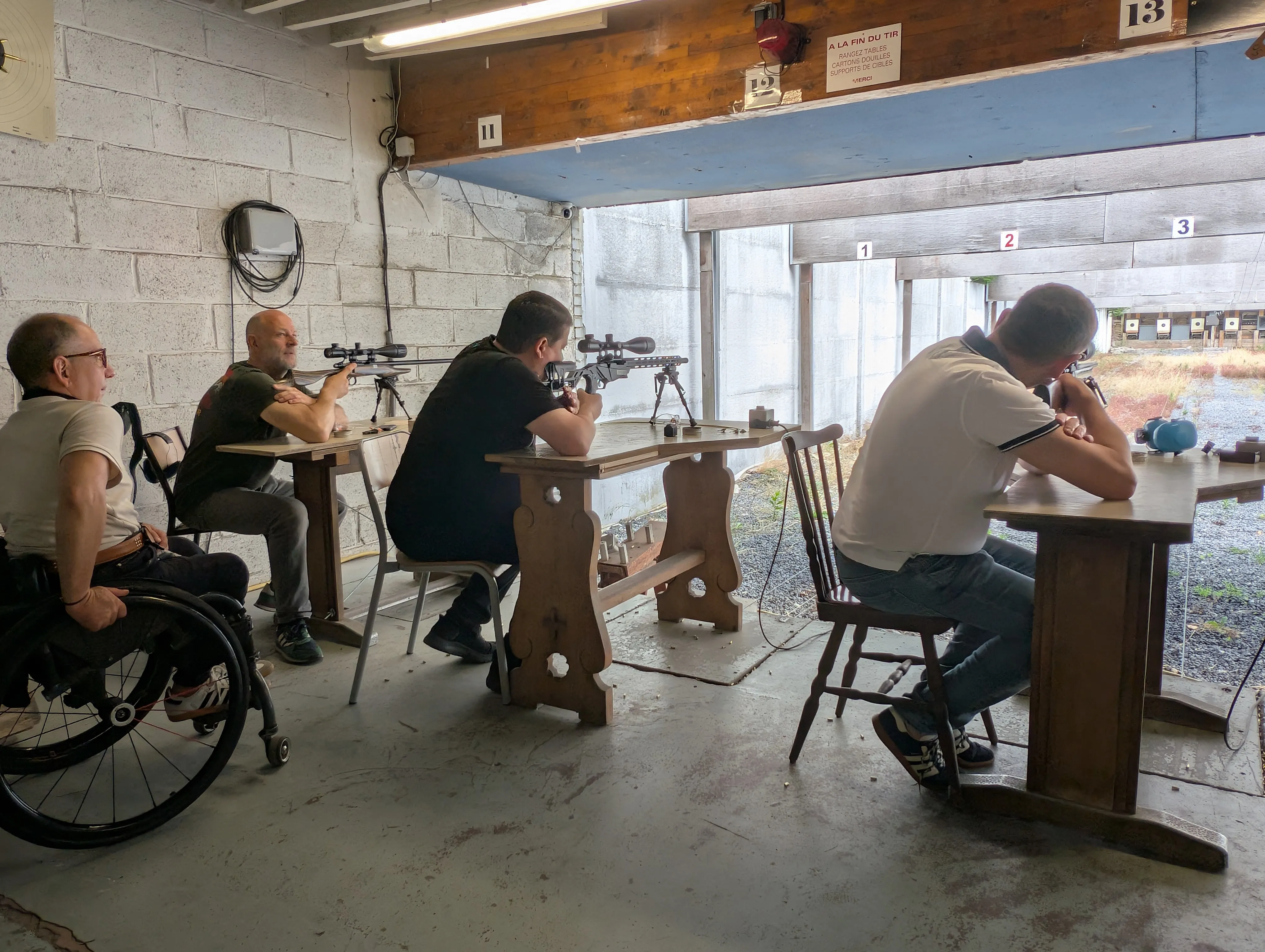 Au stand 50 m, quatre adhérents de générations différentes tirent côte à côte, dont un tireur en fauteuil