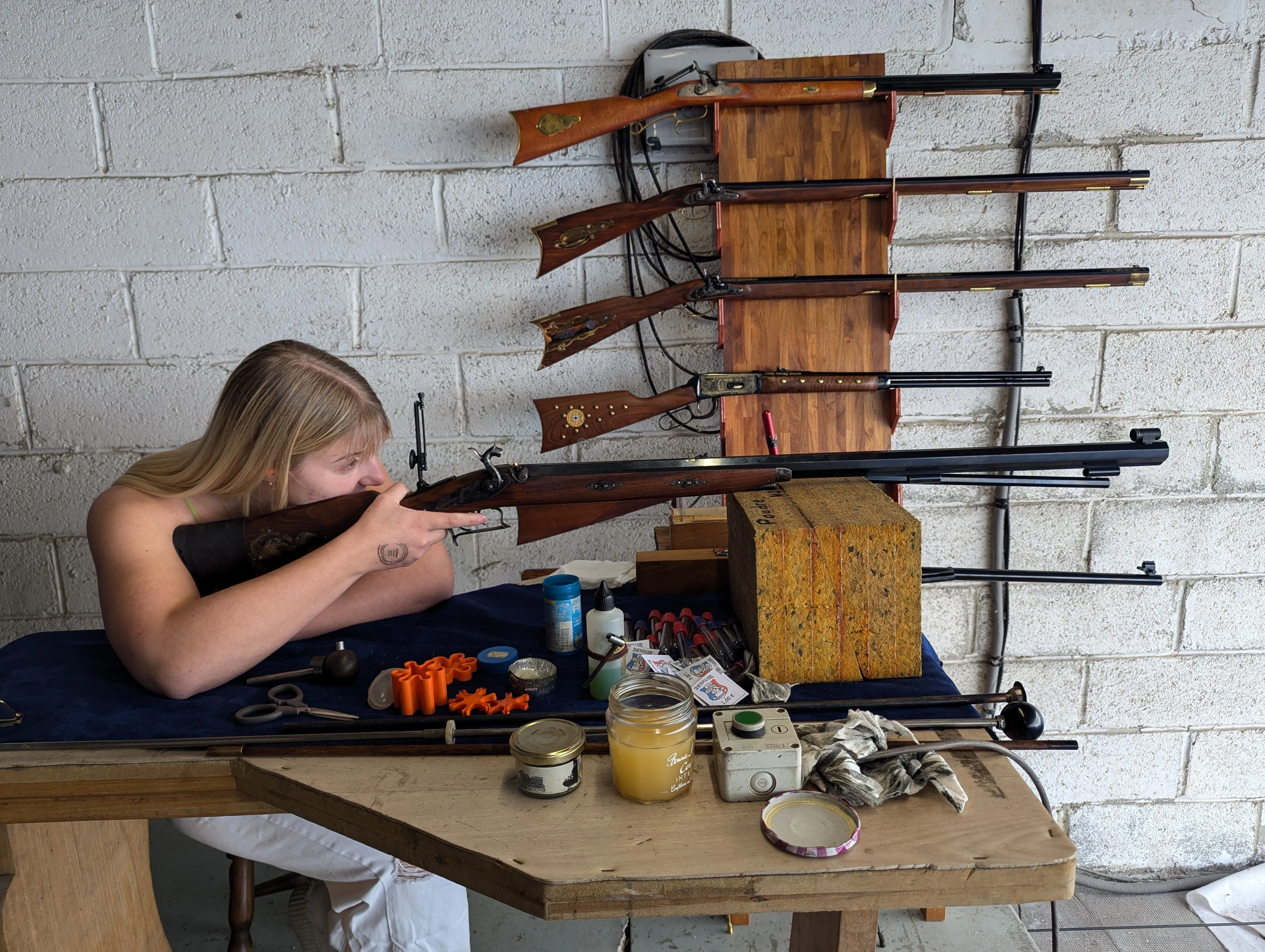 Une adhérente vise au fusil à poudre noire, devant le râtelier des armes anciennes